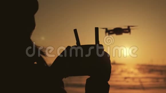 女孩用遥控操作无人机剪影女无人驾驶飞机在日落视频的预览图