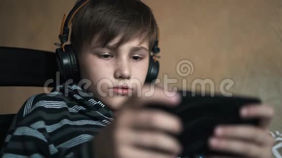 特写男孩在耳机上听音乐10岁的孩子喜欢坐在床上的智能手机视频的预览图