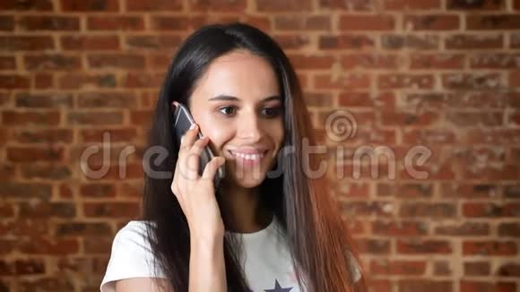 年轻可爱的女孩在智能手机上交谈对话背景砖墙肖像视频的预览图