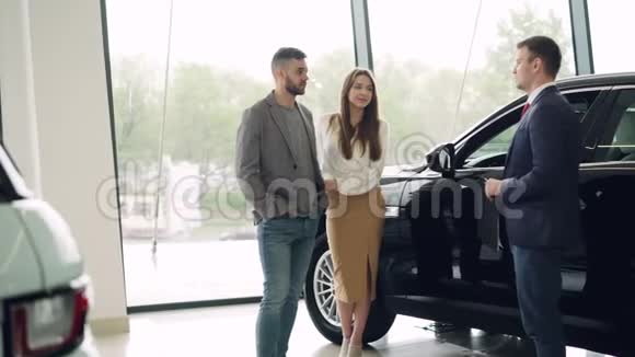 这对漂亮的情侣正在和豪华汽车经销商的汽车销售经理交谈看着漂亮的黑色汽车视频的预览图