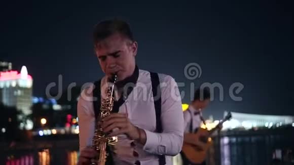 萨克斯演奏家在大城市的夜间长廊上演奏街头音乐家在观众面前的表演视频的预览图