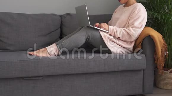 快乐女孩在家坐在现代沙发上用笔记本电脑视频的预览图