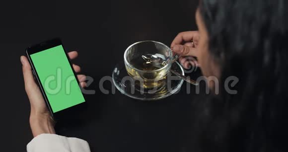 年轻的商务女性使用带有绿色屏幕的智能手机喝茶触摸屏上黑色智能手机绿色屏幕女孩视频的预览图