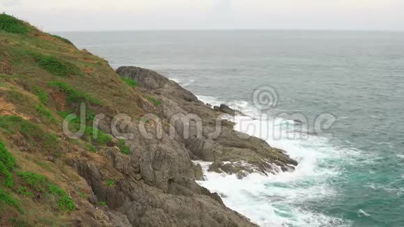 在热带海洋的蔚蓝的水面上波浪一个有岩石海岸和绿色植物的岛屿视频的预览图