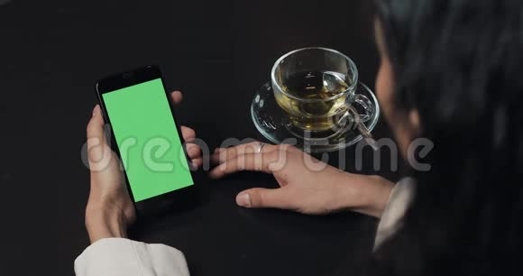 年轻的商务女性使用带有绿色屏幕的智能手机喝茶触摸屏上黑色智能手机绿色屏幕女孩视频的预览图