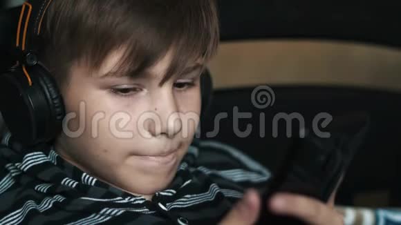 一个快乐的十几岁男孩躺着拿着智能手机和耳机在家听音乐儿童休息视频的预览图