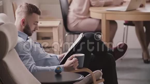 年轻成功的白种人商人坐在扶手椅上阅读文件在办公室喝着杯子里的咖啡视频的预览图