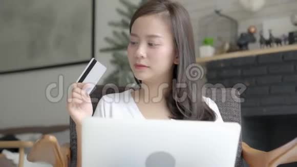 美丽的肖像年轻的亚洲妇女在网上购物用笔记本电脑上网坐在家里的客厅里视频的预览图