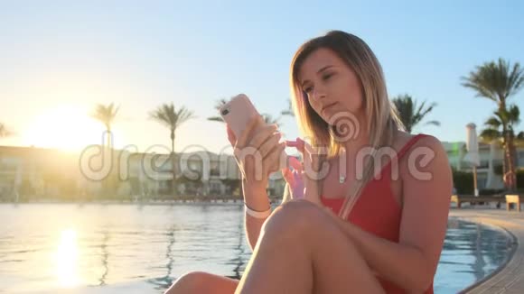 迷人的年轻女孩穿着红色泳衣在游泳池附近的智能手机上交谈的肖像比基尼女孩视频的预览图