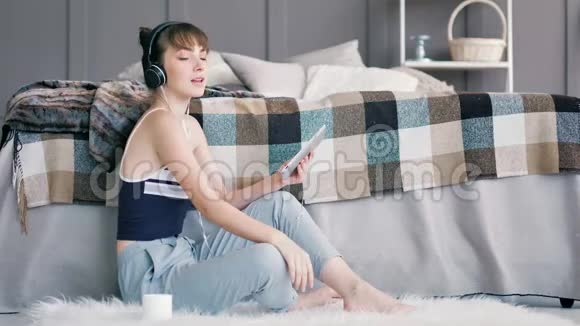年轻开朗的青少年女性在家中使用平板电脑享受耳机音乐视频的预览图