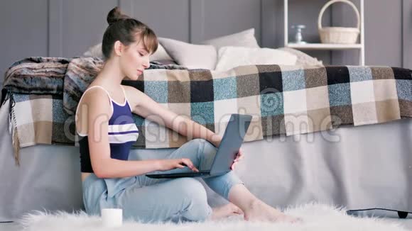坐在蓬松的白色地毯上使用笔记本电脑的年轻迷人的女性青少年的侧视图视频的预览图