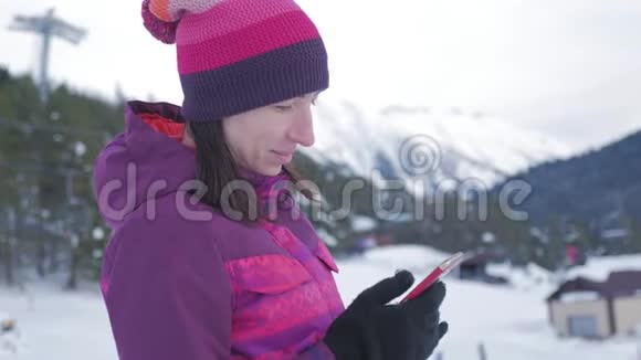 有魅力的年轻女子在一个滑雪胜地站在雪地上用手机视频的预览图