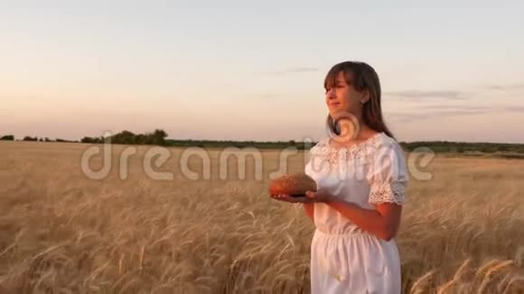 年轻女子手掌上的美味面包女孩手捧面包穿过成熟的麦田视频的预览图