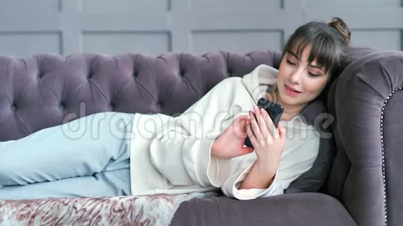 少女躺在客厅的沙发上用智能手机聊天写信息视频的预览图