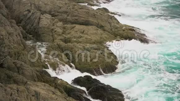 海浪撞击岩石海岸白色的海水泡沫滴落在岩石上视频的预览图