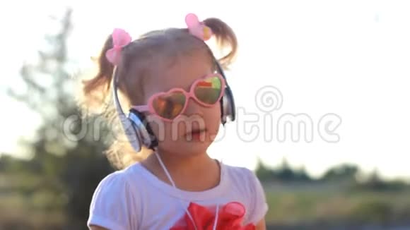 戴耳机的搞笑孩子听音乐唱歌跳舞夏天日落时戴太阳镜的可爱女孩视频的预览图