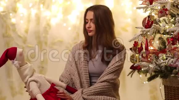 年轻的女人带着格子的微笑拥抱圣诞老人的手坐在圣诞树旁边视频的预览图