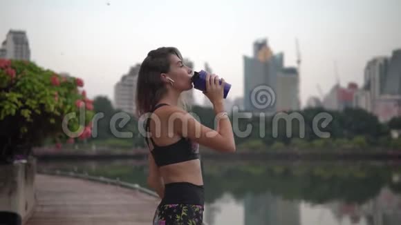 年轻的深色头发的女人在公园锻炼后喝健身饮料视频的预览图