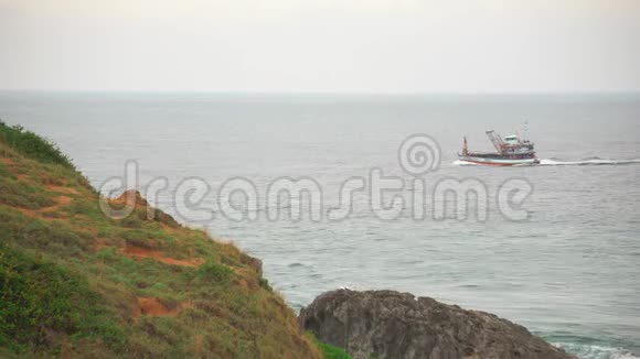 钓鱼或货船平静地漂浮在海洋水域岩石海岸的前景视频的预览图