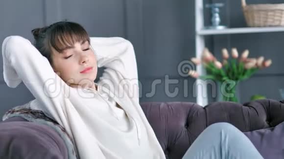 疲惫放松的年轻女性双手伸展坐在沙发上穿着舒适的毛衣在家里视频的预览图