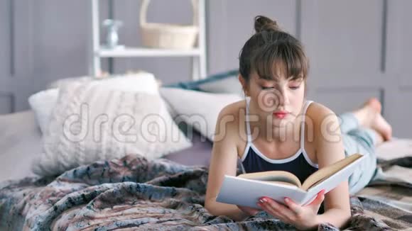 躺在肚子上光着脚躺在床上看书的漂亮黑发女孩视频的预览图