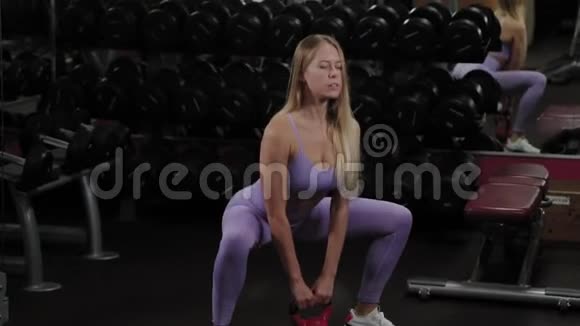 有着美丽身材的运动女人正在健身房里用水壶铃训练视频的预览图