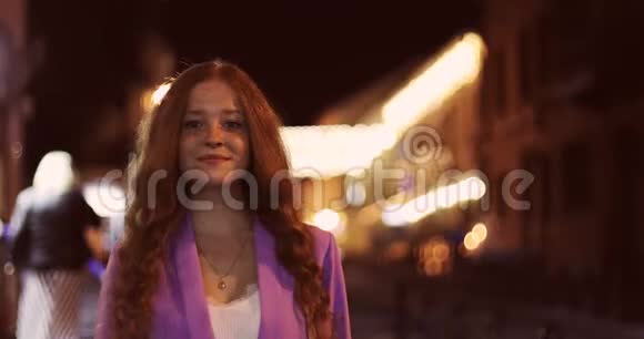幸福的女孩留着红色卷发的肖像走在夜城里视频的预览图