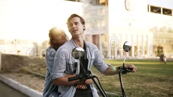 一对漂亮夫妇坐在自行车上的概述镜头女孩从后面拥抱男人穿着黑色T恤视频的预览图