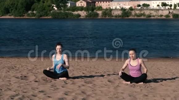 两个女人在城市河边的海滩上做瑜伽聊天美丽的景色视频的预览图