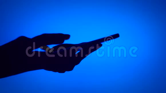 黑色轮廓女性手影使用智能手机触摸屏上的蓝色背景打字信息视频的预览图