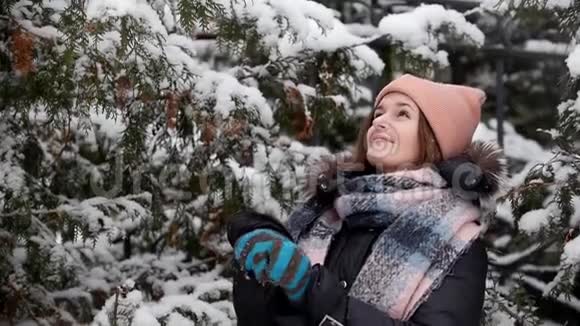 快乐的年轻女子摇动树枝雪花从树上飘落视频的预览图