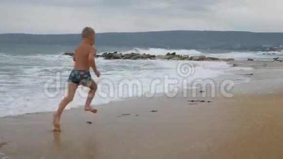 晒黑的男孩在金色的沙滩上沿着海岸奔跑视频的预览图