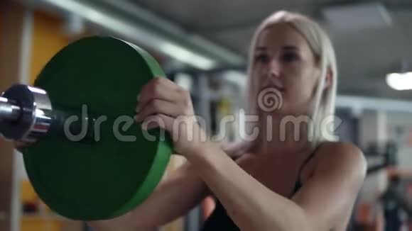 适合金发女孩在健身房把重量轮在酒吧锻炼准备健身房的训练视频的预览图