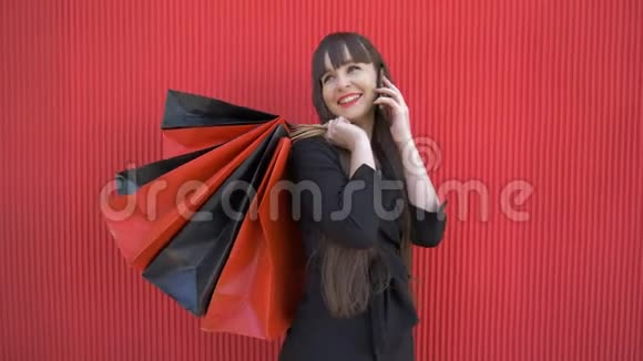 购物后的快乐女孩在手机上交流并在黑色星期五在红色上持有大量包裹视频的预览图