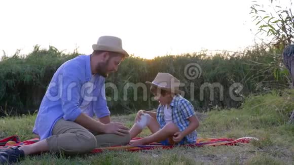 受伤膝盖上有绷带的农村孩子正坐在爸爸旁边戴着草帽竖起大拇指视频的预览图