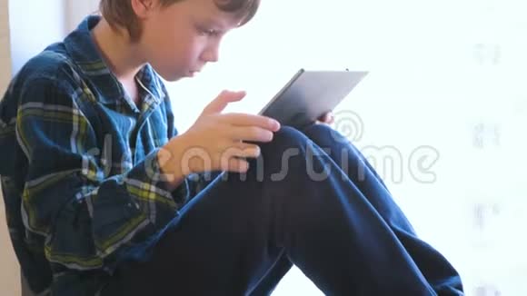 性感的男孩正坐在窗台上看平板电脑上的视频视频的预览图