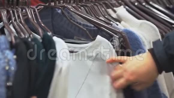 女人双手穿过一排衣服在一家精品店里浏览视频的预览图