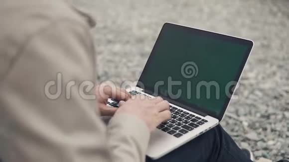 近距离拍摄一名男子的手他在户外的岩石海滩上使用笔记本电脑视频的预览图