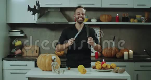 年轻有魅力的男人在厨房里玩刀准备万圣节派对美丽的万圣节装饰品视频的预览图