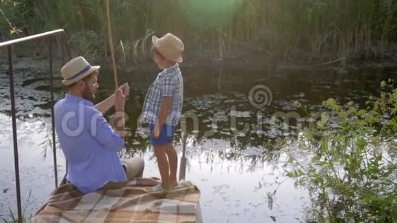 一家人钓鱼快乐的爸爸和戴着草帽的孩子在度假时在湖边钓鱼然后爸爸伸出大拇指视频的预览图