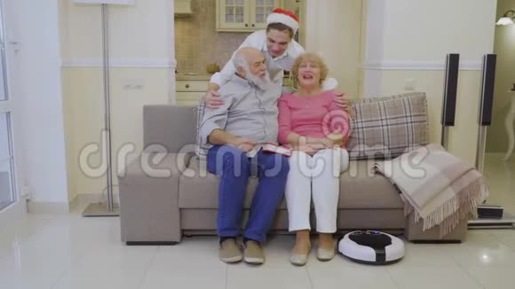 年轻人戴着圣诞老人帽子拥抱祖父母幸福的家庭显示大拇指视频的预览图