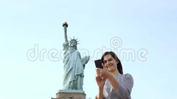 美丽快乐的白种人旅游妇女在纽约市自由女神像与智能手机拍摄自拍照片视频的预览图