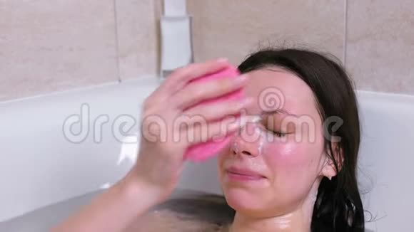 女人用面罩上的海绵洗脸然后躺在浴室里擦洗视频的预览图