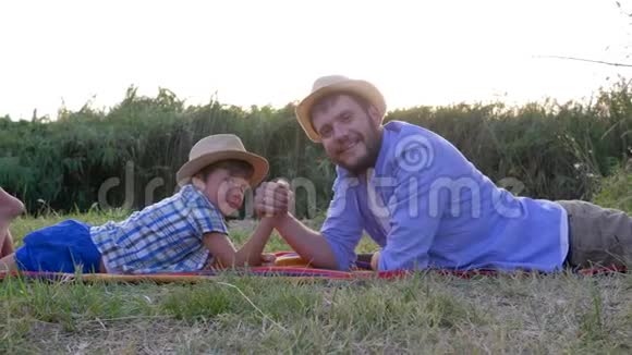 在乡村夕阳的映衬下幸福的父子俩在户外躺在格子花格子上一起玩摔跤视频的预览图