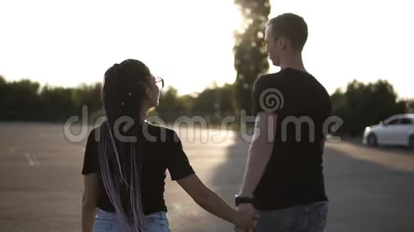一个穿着黑色T恤的男人和一个穿着黑色衬衫的女孩带着可怕的人走在停车场旁恋爱中的情侣太阳视频的预览图