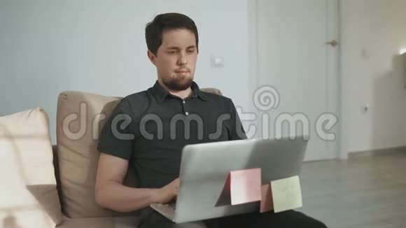 成年男子在公寓里的笔记本电脑上做自由职业者那里只猫视频的预览图