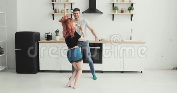 快乐的年轻夫妇穿着睡衣在厨房跳舞早上在家听音乐视频的预览图