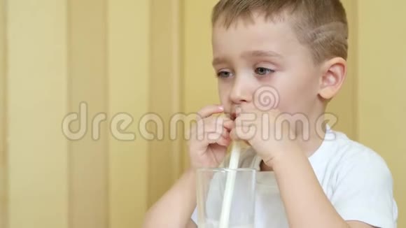 一个快乐的孩子坐在桌子旁通过吸管从杯子里喝牛奶把相机从下移到上视频的预览图