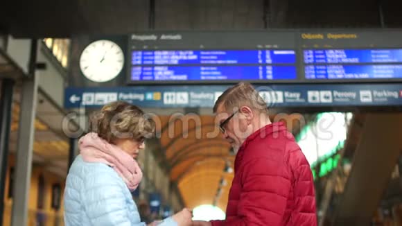 一对中年男女正在火车站台上等火车看看日程安排表视频的预览图