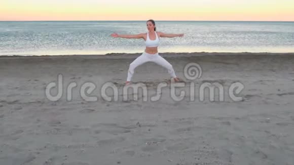 日出时坐在沙滩上做瑜伽的年轻女子在沙滩上劈叉视频的预览图
